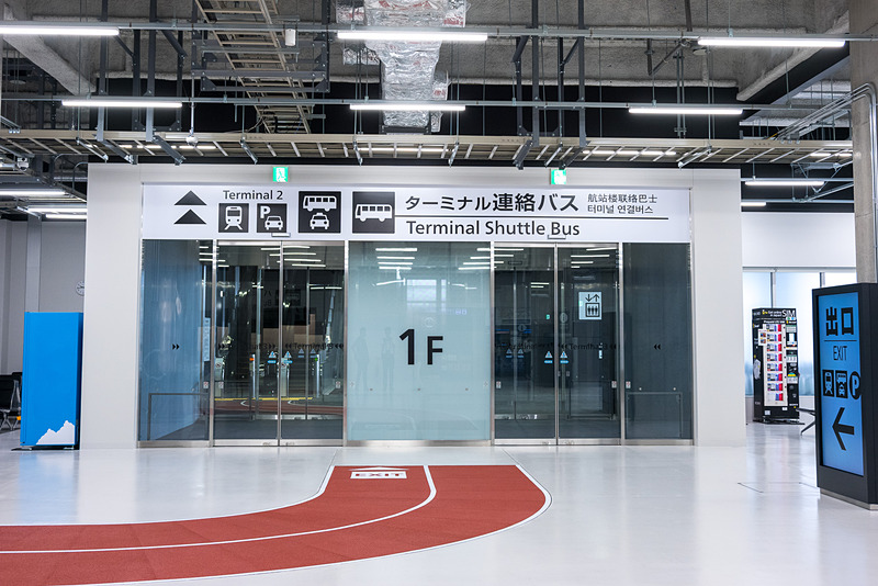出口の先に拡張された到着ロビー。赤いマットで示されたルートに沿って進むと、出発ロビーを経由せずに屋外へ。そのまま、第3ターミナルの入口に行くことができる。また従来のようにエスカレータやエレベータ、階段を使って2階出発ロビーへ行くことも可能で、この階段は従来は禁止されていた2階から1階への移動も可能になる