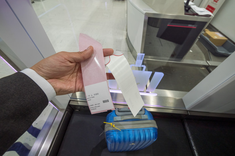 手荷物タグの貼り付け。剥離紙を剥がして取っ手などに巻き付け、シールを貼る。剥離紙側に手荷物控えが残るようになっている