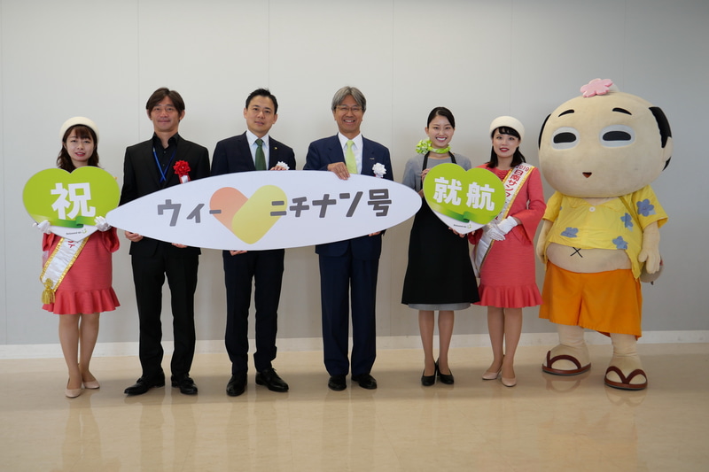 セレモニー参加者で記念撮影。左から、日南サンフレッシュレディの照井絢子さん、日南市特命大使の志伯健太郎氏、日南市長の﨑田恭平氏、株式会社ソラシドエア代表取締役社長の髙橋宏輔氏、ソラシドエアCAの空閑光咲さん、日南サンフレッシュレディの田村梨子さん、日南市観光イメージキャラクター「にちなんぢゃ様」