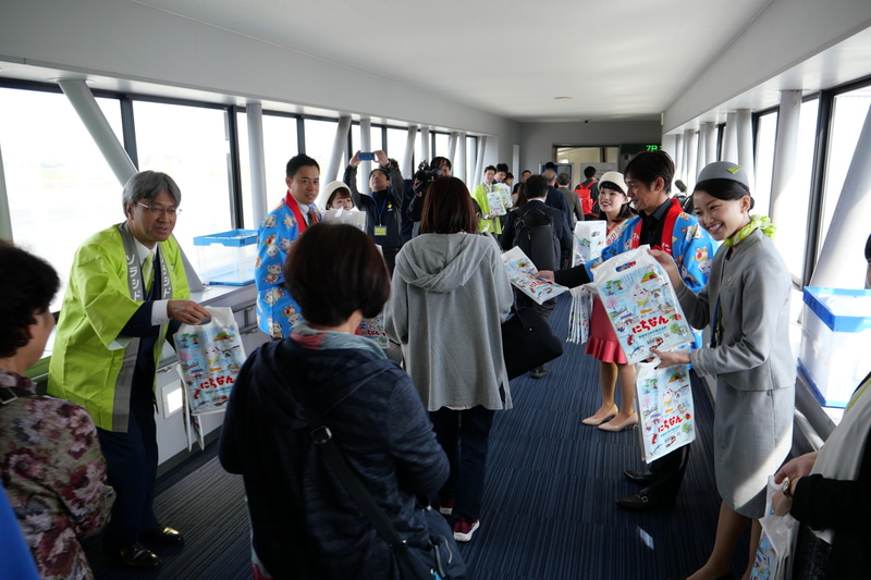 セレモニー参加者が搭乗口に並び、乗客に記念品をプレゼントした