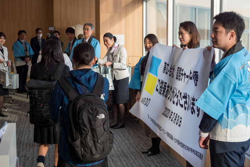 株式会社AIRDO 代表取締役社長 草野晋氏（左上）らが記念品を配布するとともに搭乗客をお見送り