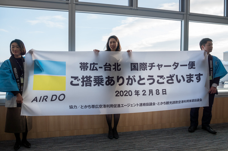 株式会社AIRDO 代表取締役社長 草野晋氏（左上）らが記念品を配布するとともに搭乗客をお見送り