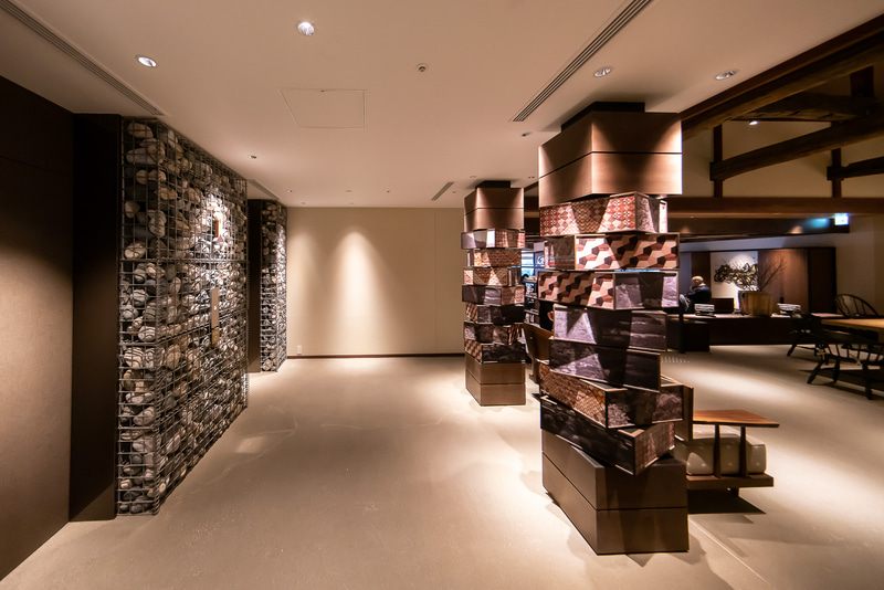 エントランスホールにあるエレベーター。川の石がモチーフに使われている。右は回転する写真が使われたアート