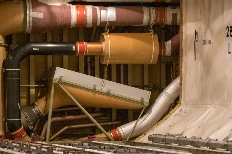 機体下部の貨物室奥（通常は壁になっており見ることはできない）に搭載しているHEPAフィルター。このダクトはマニホールドになっており、機外からの空気と、HEPAフィルターを通過した機内からの循環空気を混合し、中央の太いダクトで機体上部へと運んでいる。