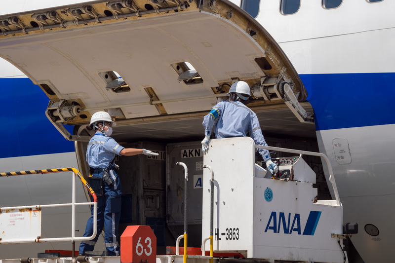 貨物を下ろす作業が進められる。ソーシャルディスタンスが確保できる屋外作業では、熱中症対策のためにマスクを外すことを推奨している