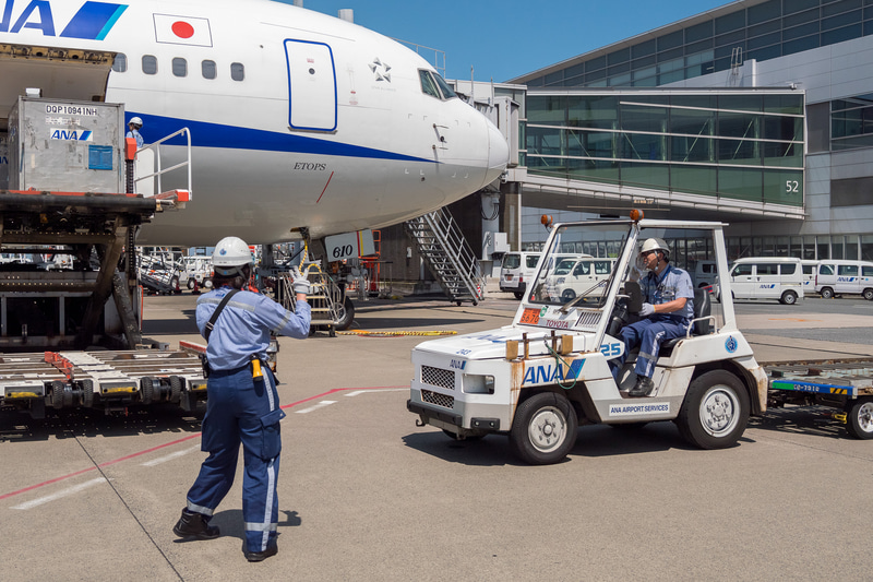 貨物を下ろす作業が進められる。ソーシャルディスタンスが確保できる屋外作業では、熱中症対策のためにマスクを外すことを推奨している