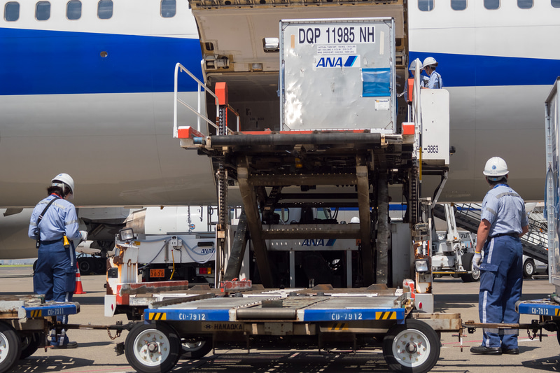 貨物を下ろす作業が進められる。ソーシャルディスタンスが確保できる屋外作業では、熱中症対策のためにマスクを外すことを推奨している