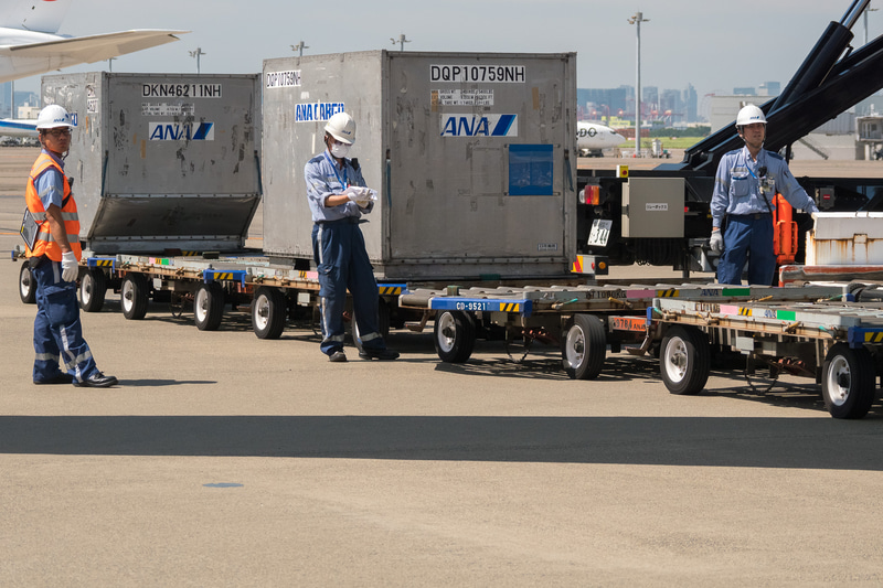 貨物を下ろす作業が進められる。ソーシャルディスタンスが確保できる屋外作業では、熱中症対策のためにマスクを外すことを推奨している