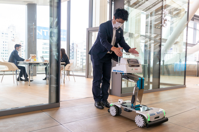 Lifter付きSEED-Mover。開発元はTHK。軽食や飲料の運搬を想定したパーソナルサイズの小型配膳ロボット。この日は2階の通路から3階のミーティングスペースの前までホットコーヒーを運搬。フロア移動に使うエレベータは自動で乗り降りする（エレベータの操作は手動）