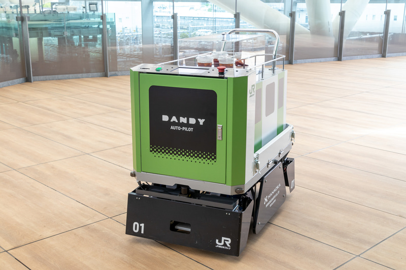 DANDY AUTO-PILOT。開発元は花岡車輌。山手線をイメージした小型搬送ロボットで、軽食や飲料を目的地まで運ぶ。3階の通路からミーティングスペースの前までアイスコーヒーを運搬した