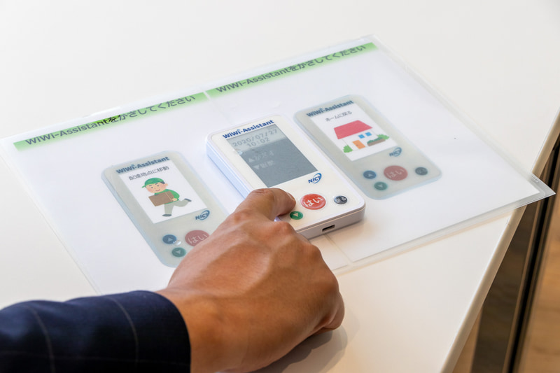 FRUTERA（フルテラ）。開発元はアンドロボティクス。軽食や飲料を目的地まで運ぶ搬送ロボットで、通信障害に強いWi-SUN無線通信を採用しているのが特徴。ミーティングスペースに準備された操作ボタンを押すと、通路に待機していた本機がスペース内のテーブル近くまでお菓子を運搬。終了操作をすると自動的に転回して元の位置まで戻った