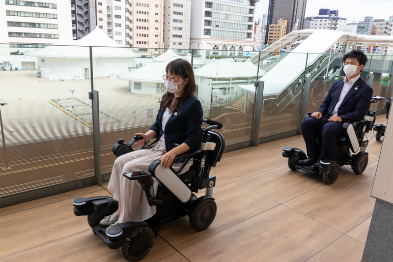 WHILL NEXT。開発元はパナソニック。車体はWHILLの「Model A」で、パナソニックの衝突防止機能を搭載したモデル。車いすタイプのパーソナルモビリティで、先頭車両を自動で追従する機能を持つ