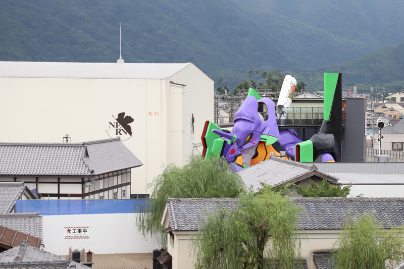 エヴァ初号機は映画村の西端にある。隣接する東映京都撮影所No. 11スタジオの壁面にNERVロゴも描かれ、巨大な京都基地を演出