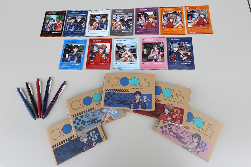 コラボグッズ。上から、2枚入りのブロマイドセット（トレーディングカード、各440円）、ボールペン（各330円）、ミニクロッキー帳（各880円）