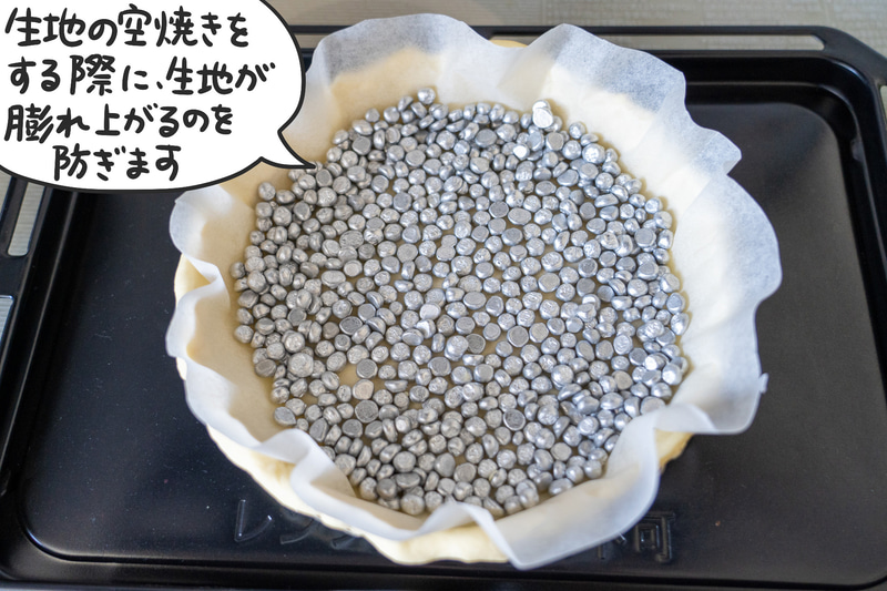 生地の上にクッキングシートを敷いてその上にタルトストーンを置き、予熱しておいたオーブンに入れます