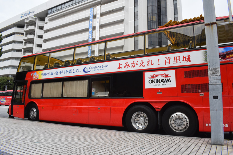 赤いボディが目を引く2階建てオープントップバス「美ら島SKY」号。「よみがえれ！首里城」のロゴが入っている