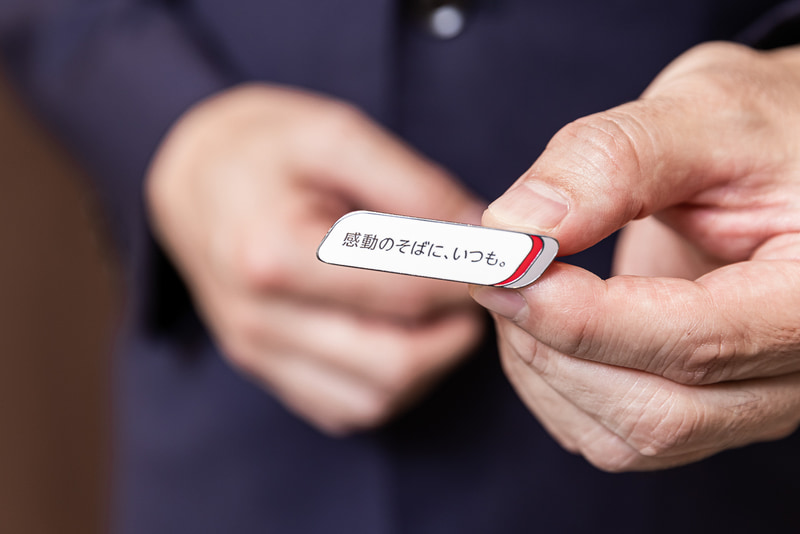 JTBグループのブランドスローガン「感動のそばに、いつも。」を掲げたバッジ