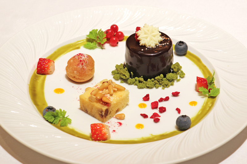 チョコレートムース 五香粉の香り、ドライフルーツ入り蒸しカステラ、杏仁クリームのプティ・シューが彩られたデザートの一皿。五香粉の香りがするめずらしいチョコレートムースなど思い出に残る一皿だ
