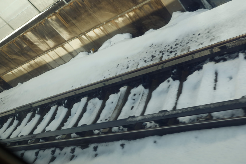 走っている車中から撮影したので不鮮明だが、レール上面より下のレベルまで雪が取り除かれている様子が分かる。ロータリーブラシ車の威力であろう