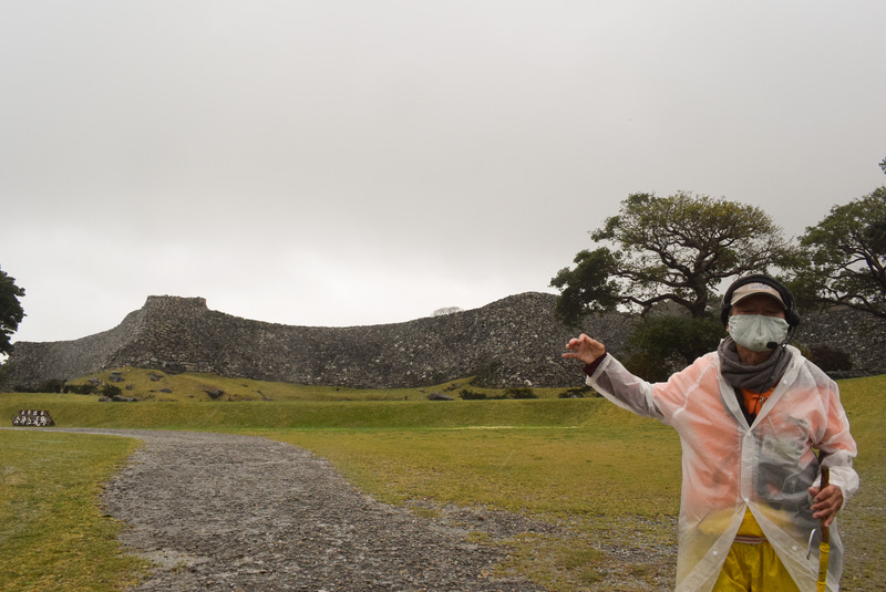 今帰仁城跡の城郭をバックに説明するガイドさん