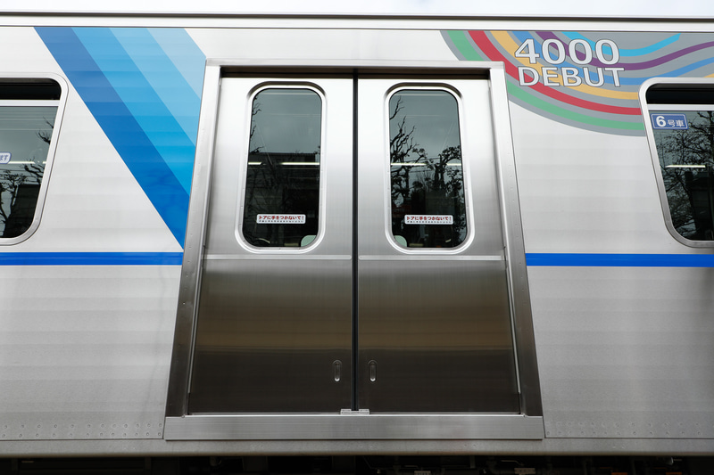 新型車両ということで記念装飾が施されているが、腰部より上に集中している。側窓より下の範囲は可動式ホーム柵に遮られていて見えないから、これでよい