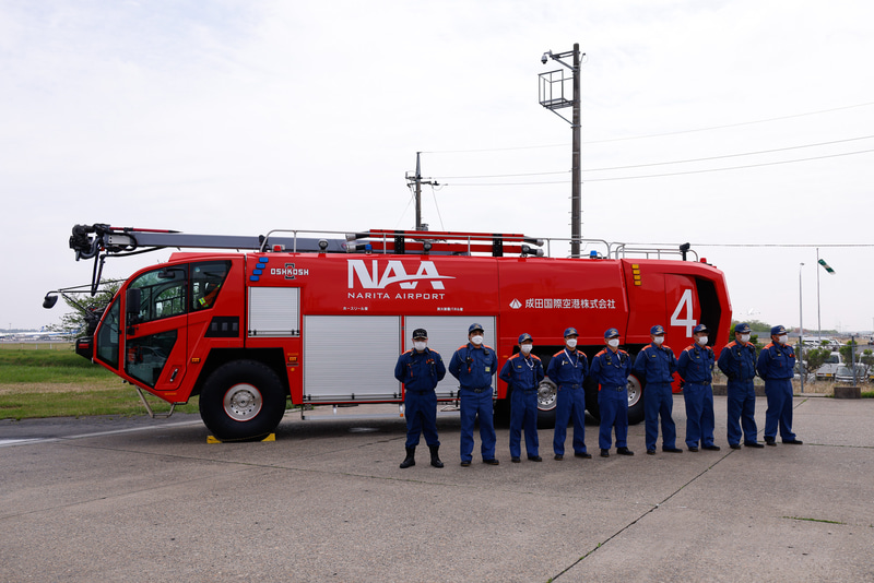 整列して出迎えた消防隊の皆さん。背後の化学消防車は、米オシュコシュ「ストライカー6×6」。航空機の火災に特化した特装車だ