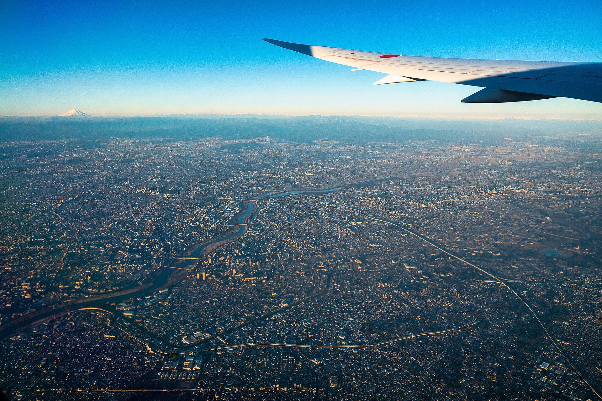 新千歳行きの左側から。東京の街並みの向こうに冠雪した富士山を望む。