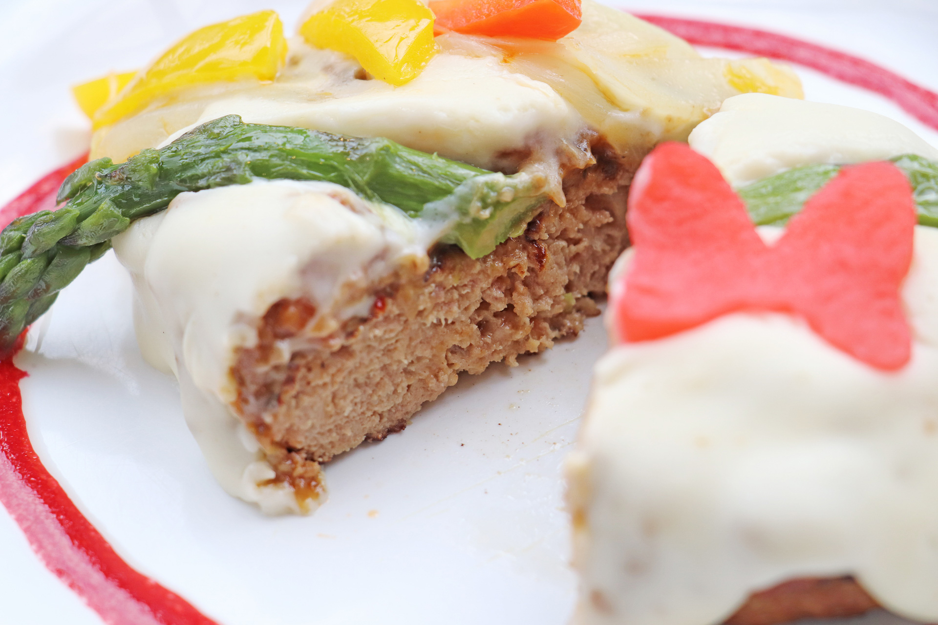 肉厚のハンバーグにマイルドなホワイトソースがたっぷり。ミニーマウスのリボン形のピクルスが乗っている