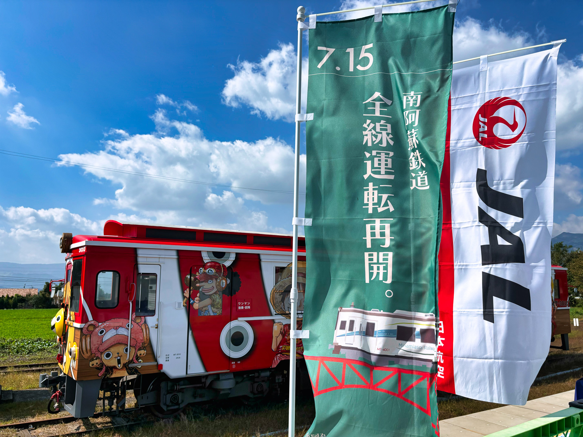 JR九州とJALとの共同企画で実施されたツアー。南阿蘇鉄道全線運転再開の幟が爽やかな風になびいていた。記念の枡と阿蘇の酒 れいざんの特別ボトルが配布された