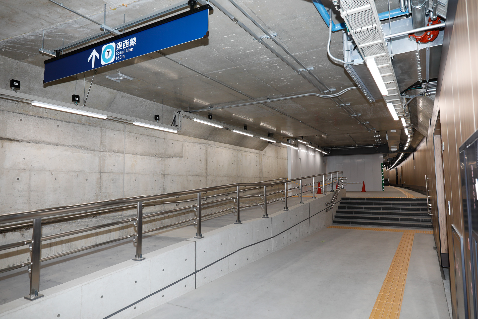 1番出口から地下に降りて改札に向かう通路。本線がカーブしているため、その上に設けられた通路もカーブしている。実は、カーブした本線のトンネル躯体と、駅施設を構成する直方体の躯体が噛み合った複雑な形状になっている。地下のことなので外からは見えないが