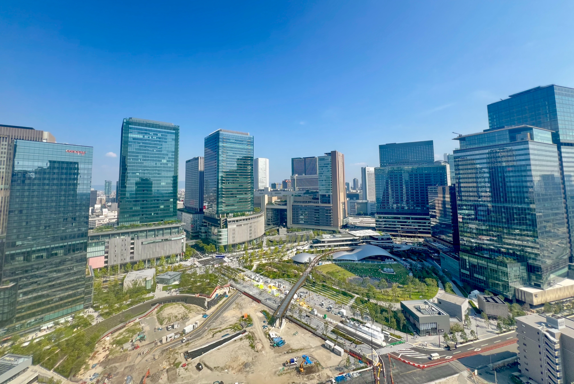 グラングリーン大阪の俯瞰全景（梅田スカイビルから、グランフロント大阪の北館/南館とJR大阪駅に向かって撮影）。写真左端ビルが北街区の北館。全体まちびらきは2027年度予定