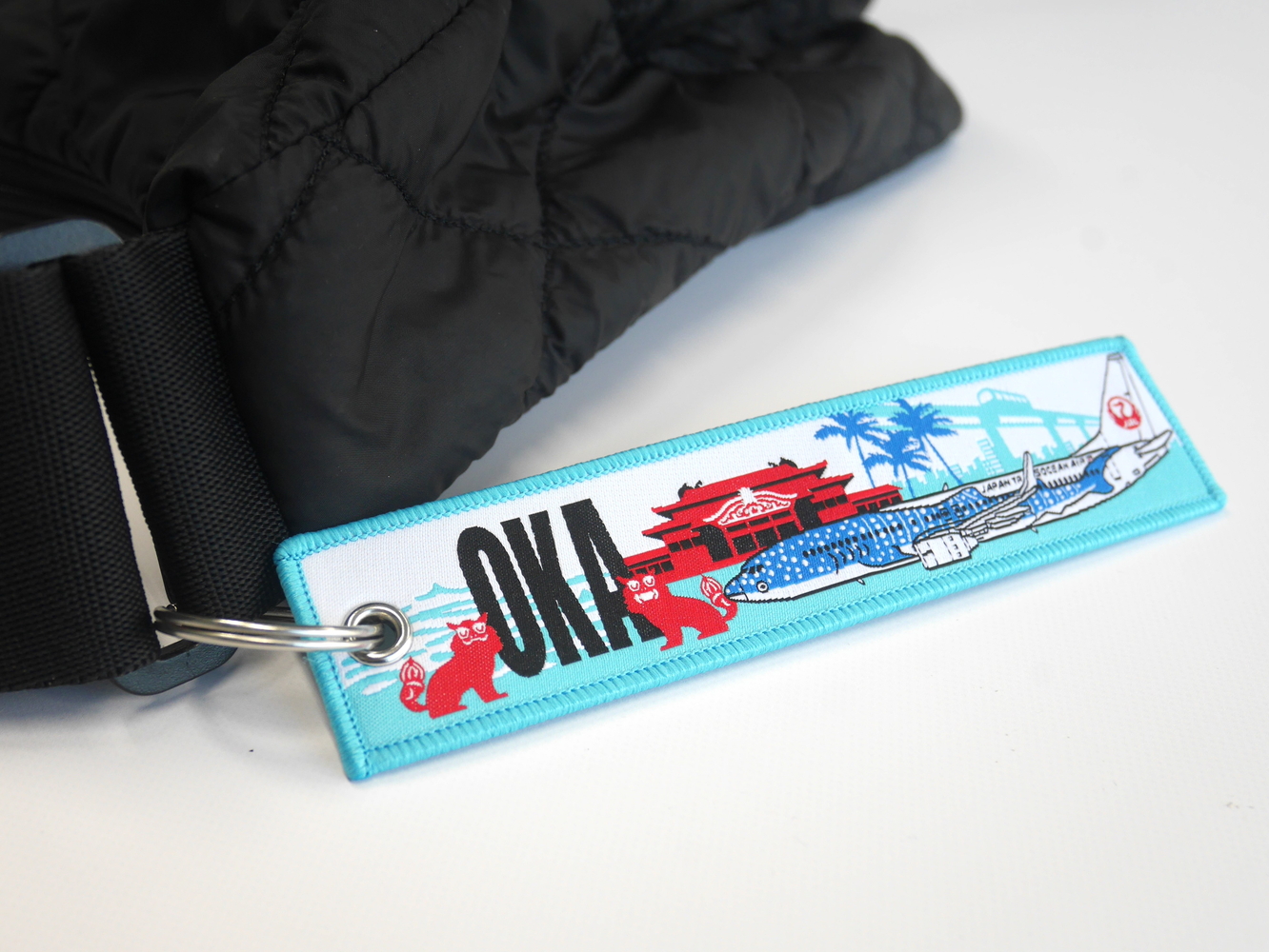 那覇空港の空港コード（OKA）や首里城、ジンベエジェットなどを描いたJTAのフライトタグキーホルダー