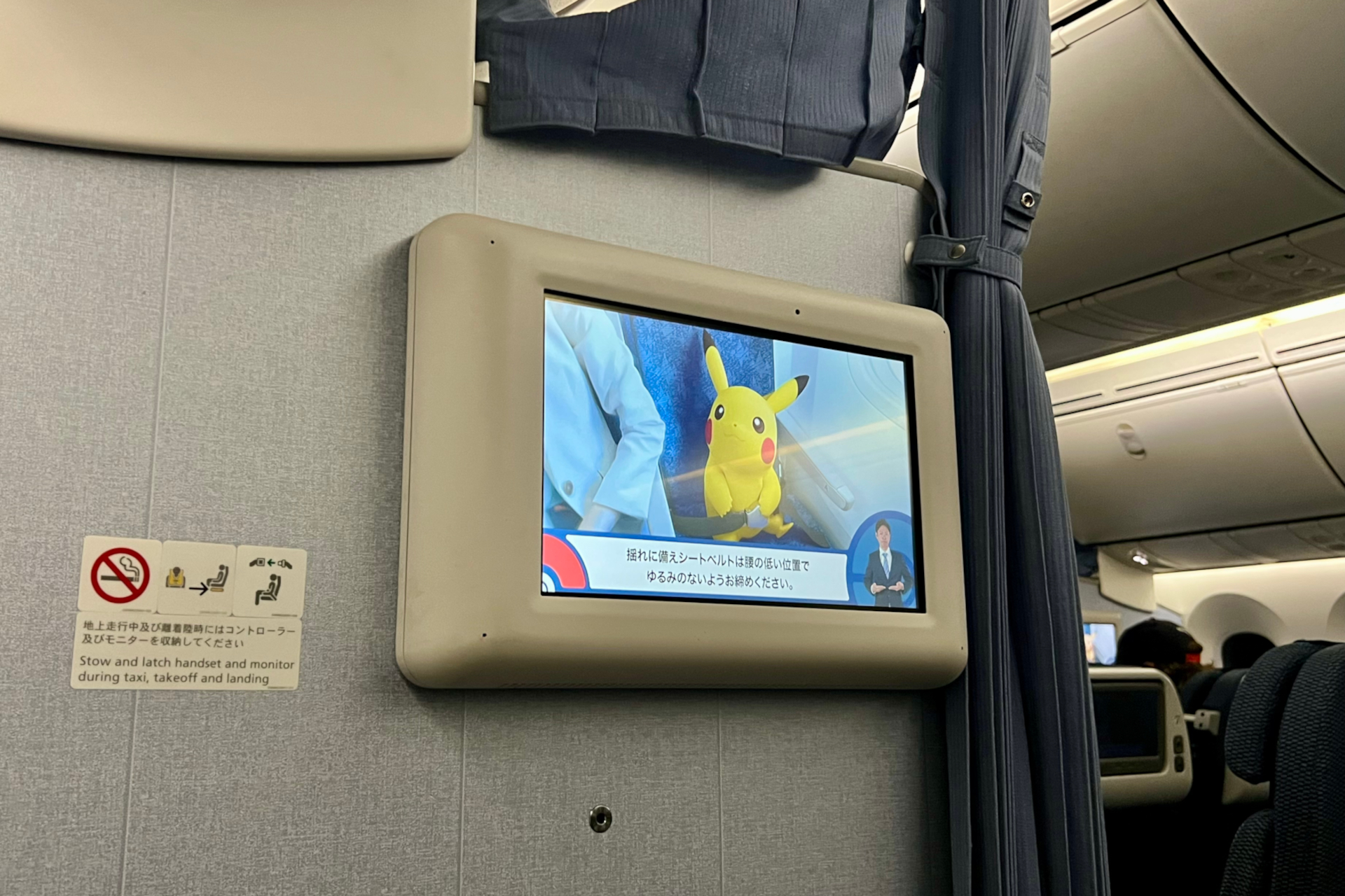 バルクヘッド席の個人モニターと食事テーブルは、アームレスト部分に格納されている。目の前の壁には機内安全ビデオやフライトマップが流れるモニターと個人専用収納ポケット