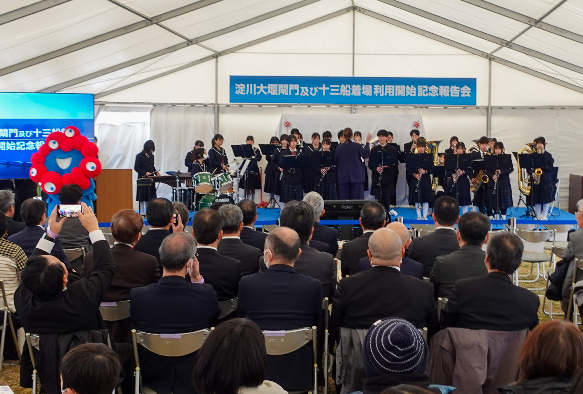 式典に登場した万博のマスコットキャラクター「ミャクミャク」と、地元・新北野中学校の吹奏楽部