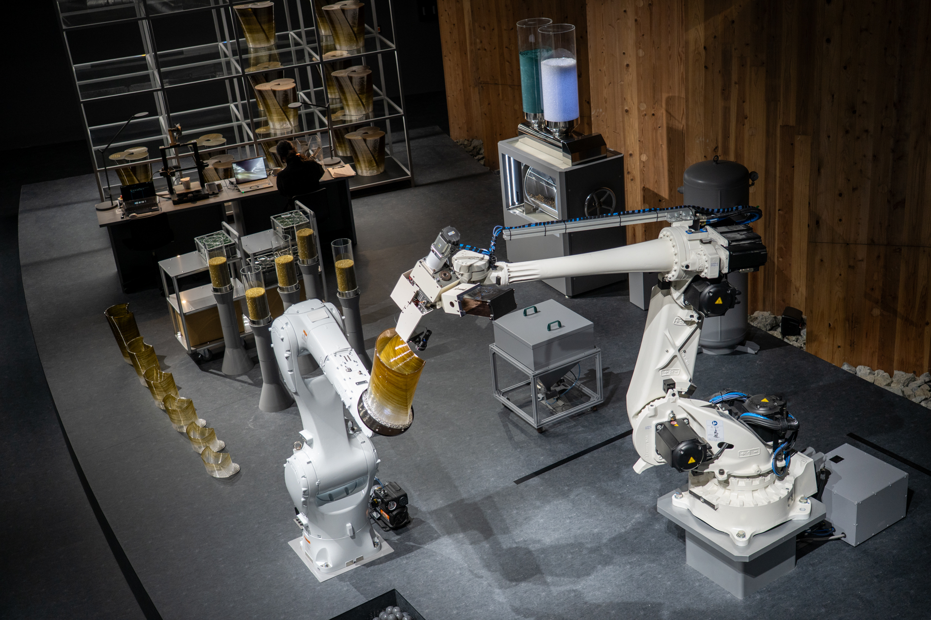 藻類を混ぜ込んだ素材を使って2機のロボットアーム型3Dプリンタがスツールを作っている様子を上から見学