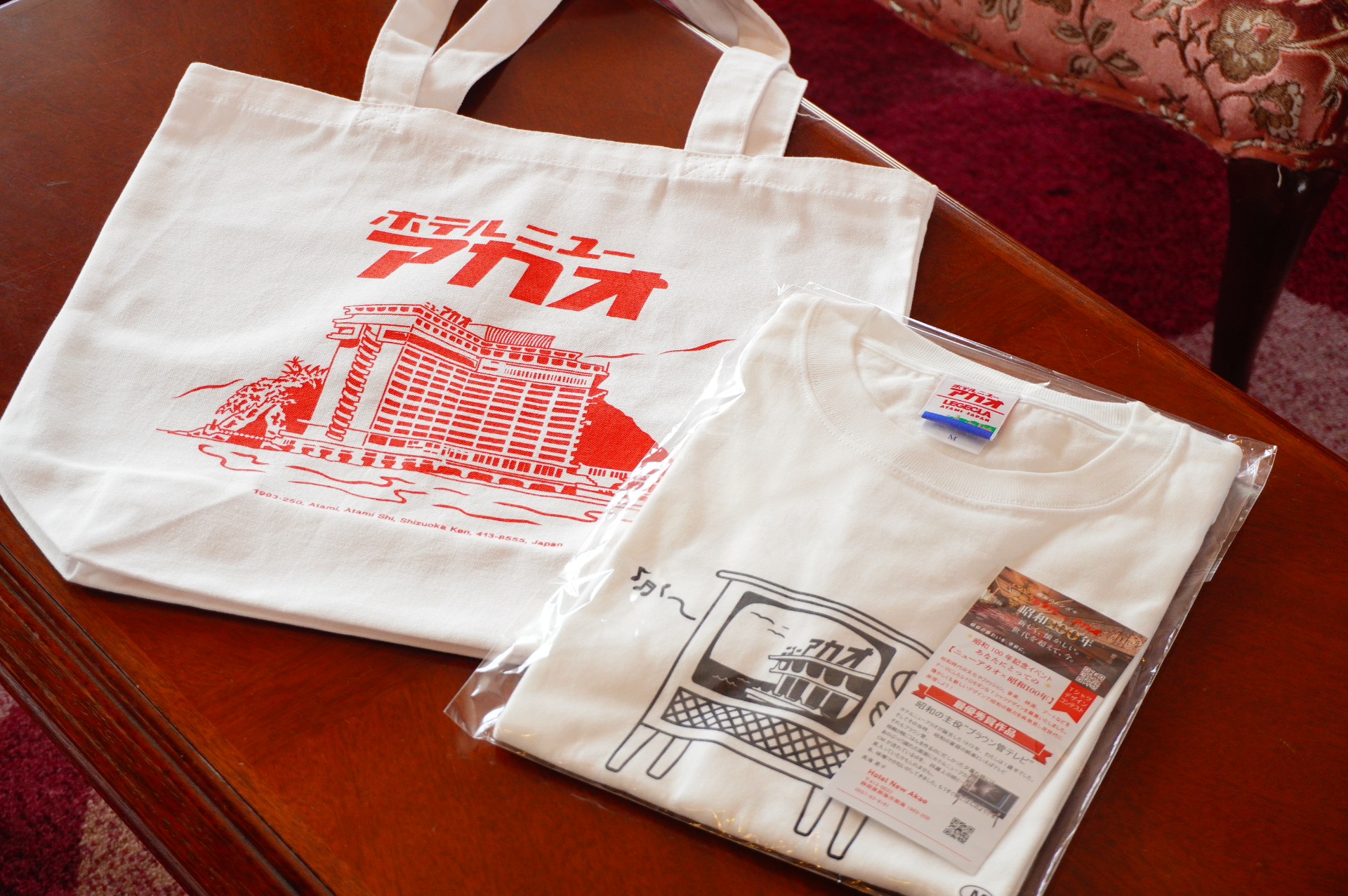 「昭和100年記念オリジナルTシャツ」（写真右）をプレゼント。ロゴTシャツやトートバッグ（写真左）などのグッズはホテルショップでも販売している