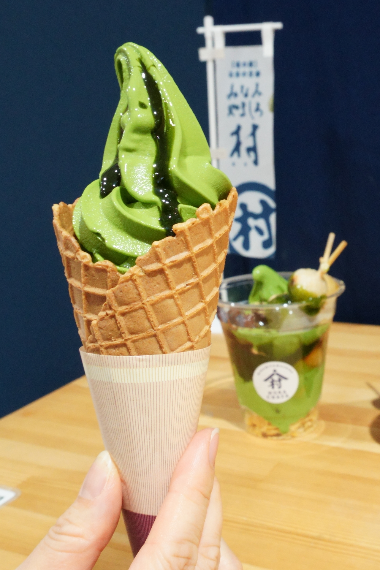 村抹茶ソフトクリーム（430円）。後ろに写っているのは「ちゃたれ～だんごパフェ」（980円）