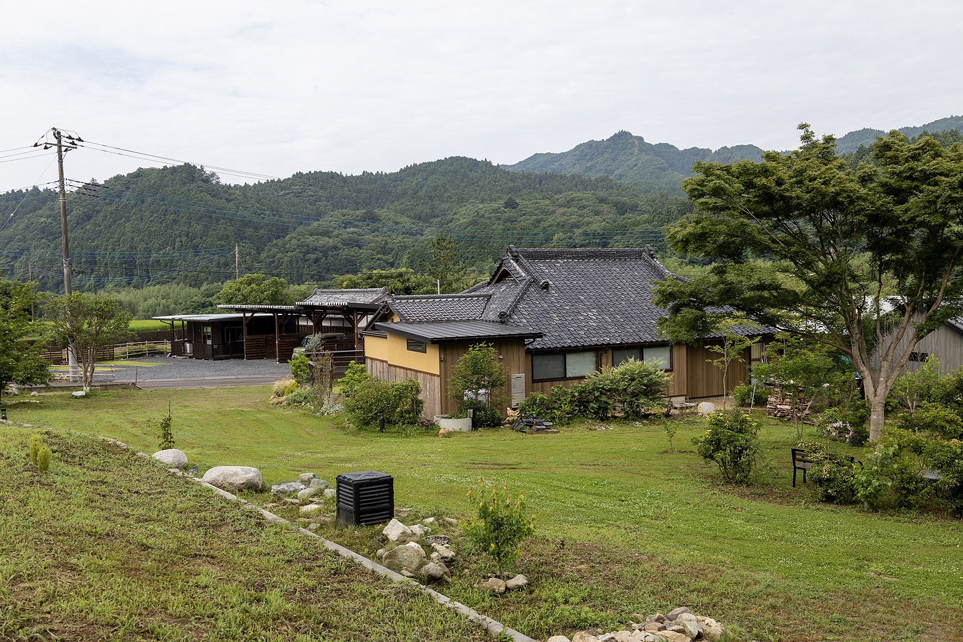 古民家裏からサイトを見る。写真奥が出入り口で、古民家の横と左側の大きな石があるところまでの壁添い（写真左より）がサイトとなる。古民家側に対してはクルマが通れるだけのスペースを取ることがルールなので、サイトでのクルマの停め方は斜めか塀に沿った横向きになるだろう
