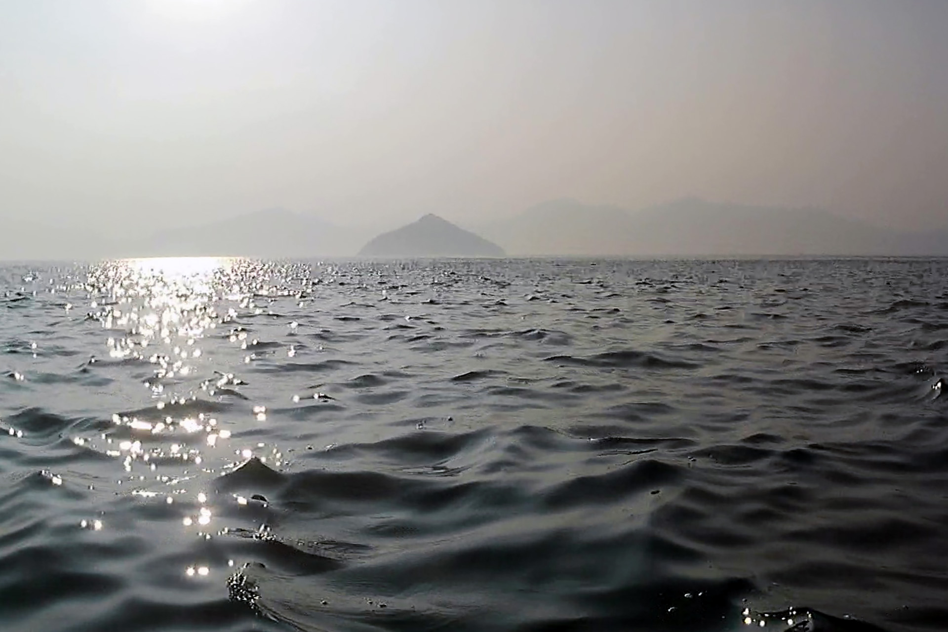 動画からの切り出しなので画質がわるいが手前に見えている小さい島は小黒神島。奥にうっすらと見えるのが厳島