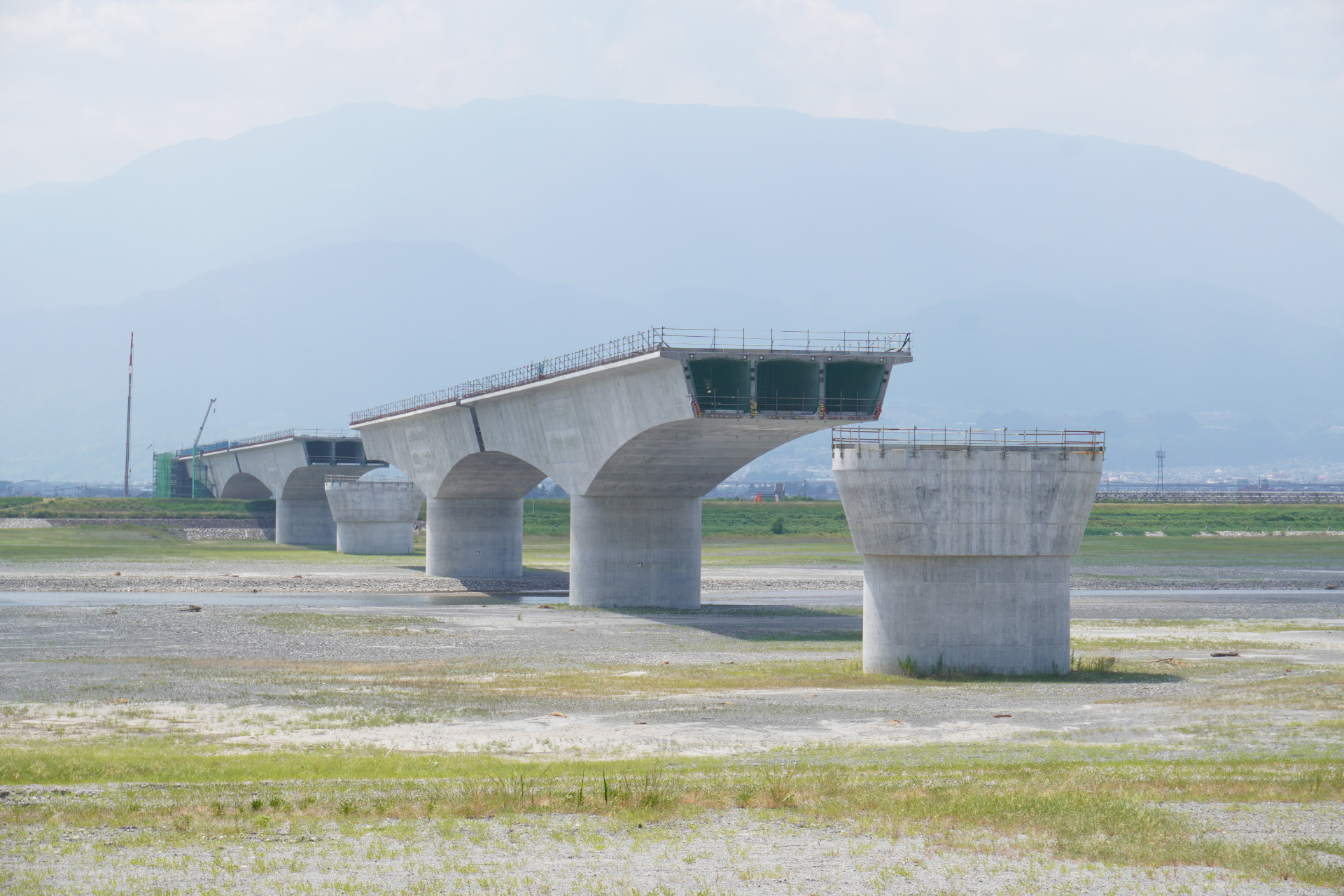 新設される山梨県駅からは西へ5kmほどの地点にある。橋を支えるためのケーソン基礎や柱の部分（下部工）は完成しており、現在は桁（上部工）をつなげていくコンクリート打設作業などを行なっている