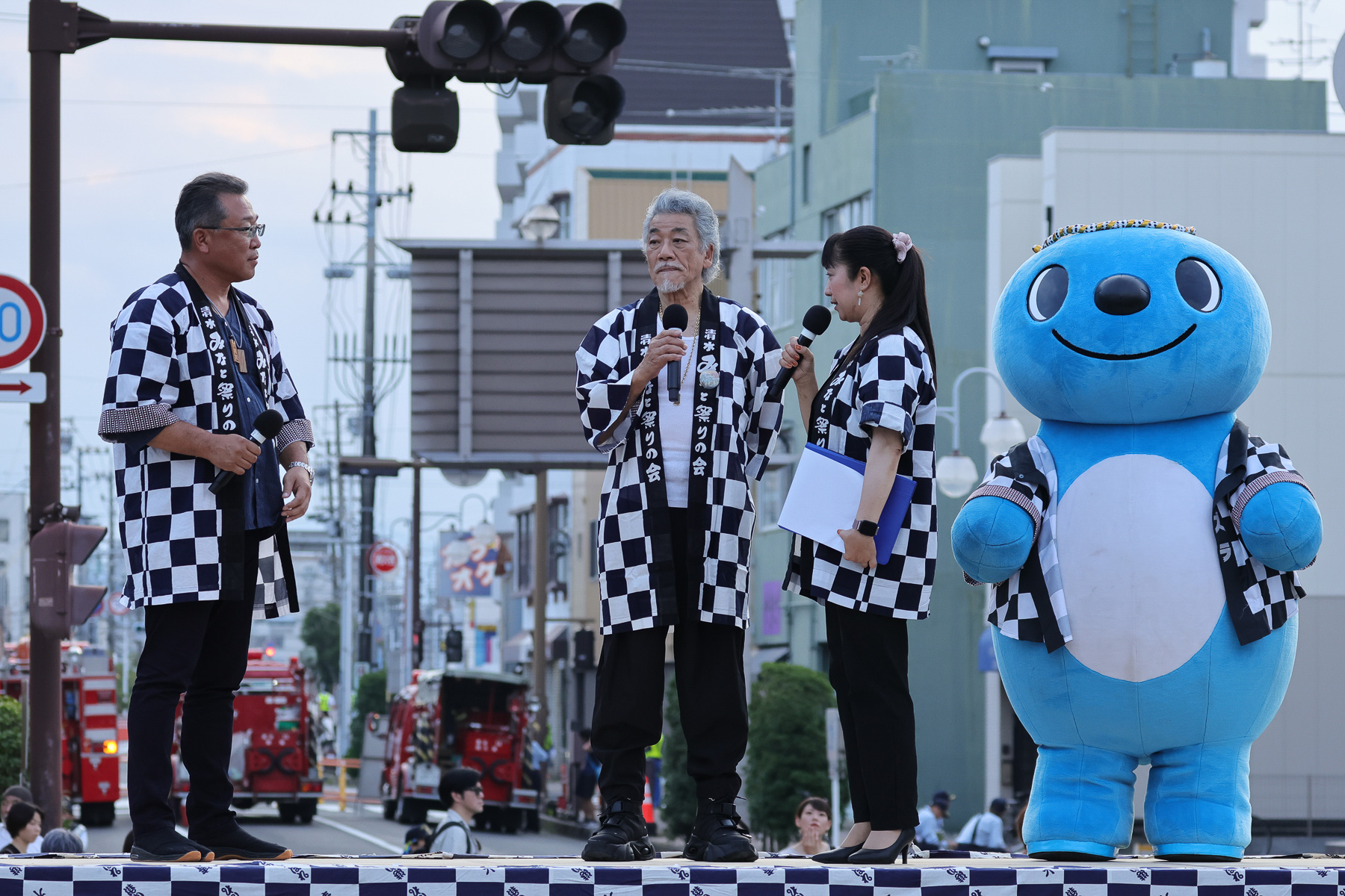 交差点上に設置した壇上でオープニングセレモニー。総おどりの曲を作詞作曲した宇崎竜童氏（中央）も登場。右端は清水区のマスコット「シズラ」