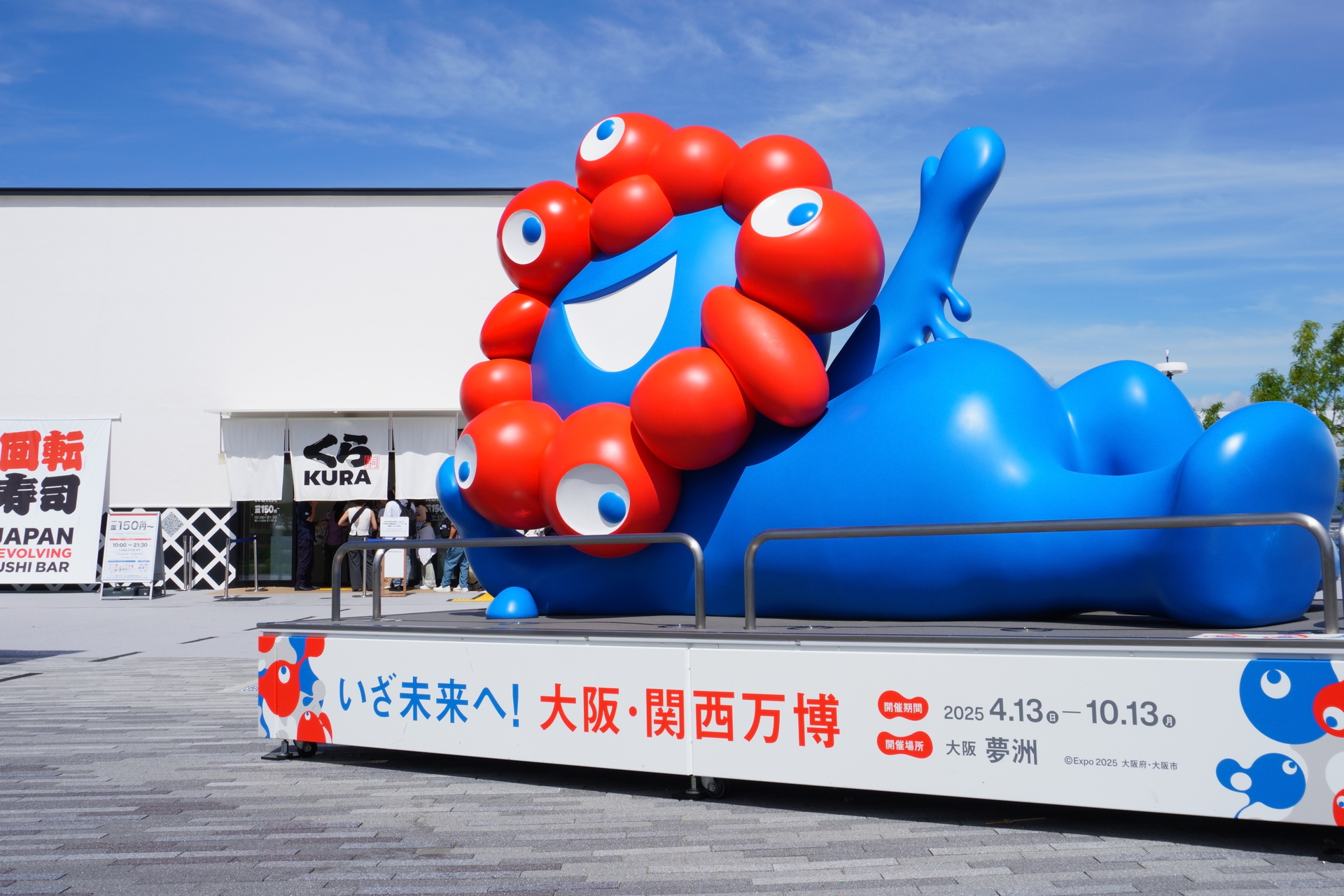 くら寿司に吸い寄せられているようにも見える、寝そべりミャクミャク像（涅槃ミャクさま）