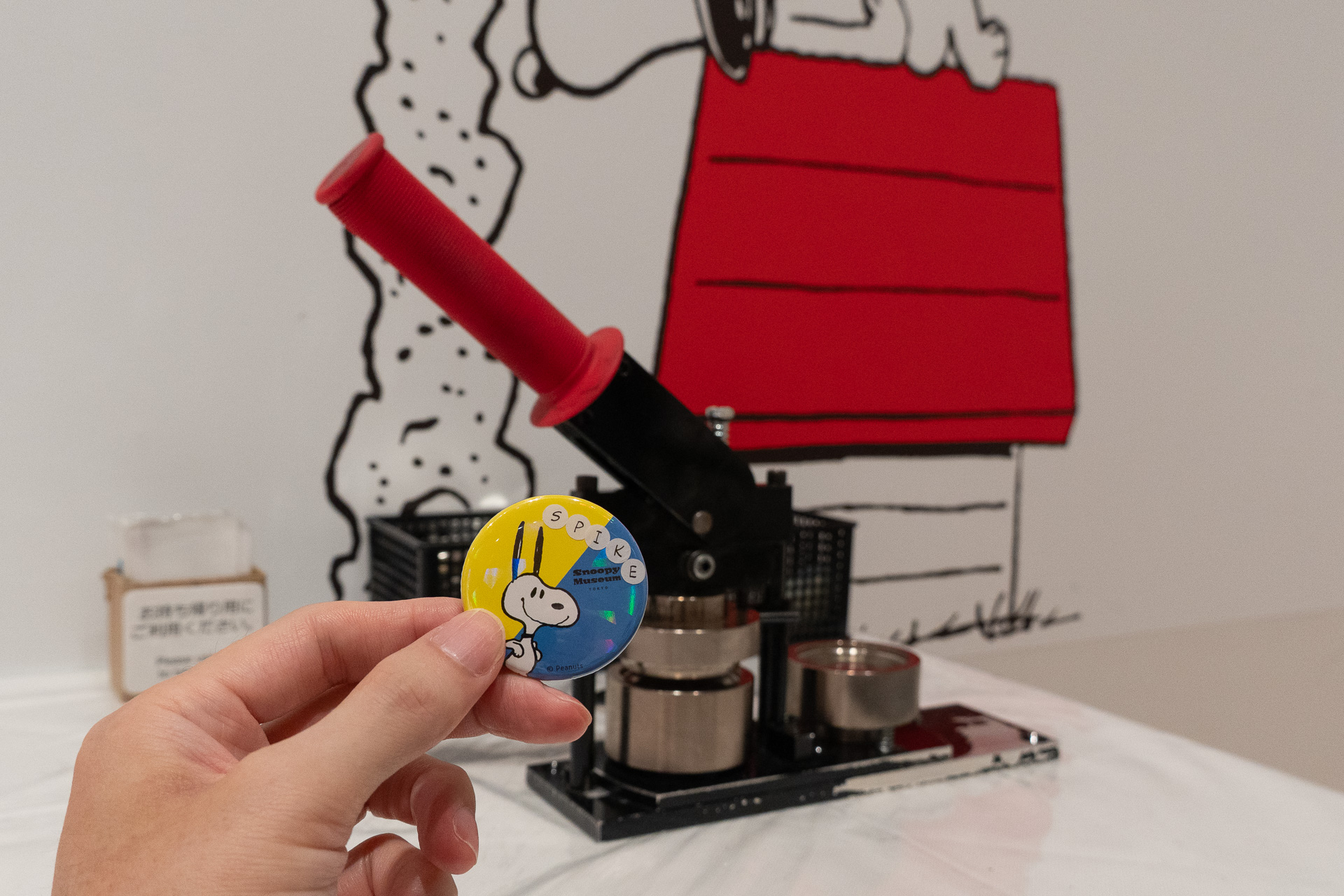 カプセルトイ自販機を回して出てきたランダムなデザインに、アルファベットシールを貼ってオリジナル缶バッジを制作できる「スヌーピー缶バッジ」（1回500円）は、ホログラム加工の新デザイン4種を追加（計10種に）