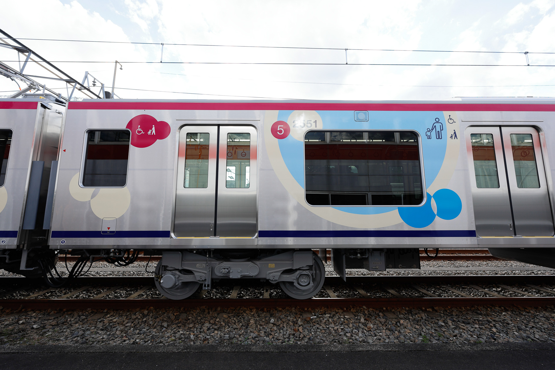 5号車の新宿寄りは、「ひだまりスペース」の存在を示す円形ラッピングとピクトグラム、それと、車端部の優先席・車椅子用フリースペースの標記がある