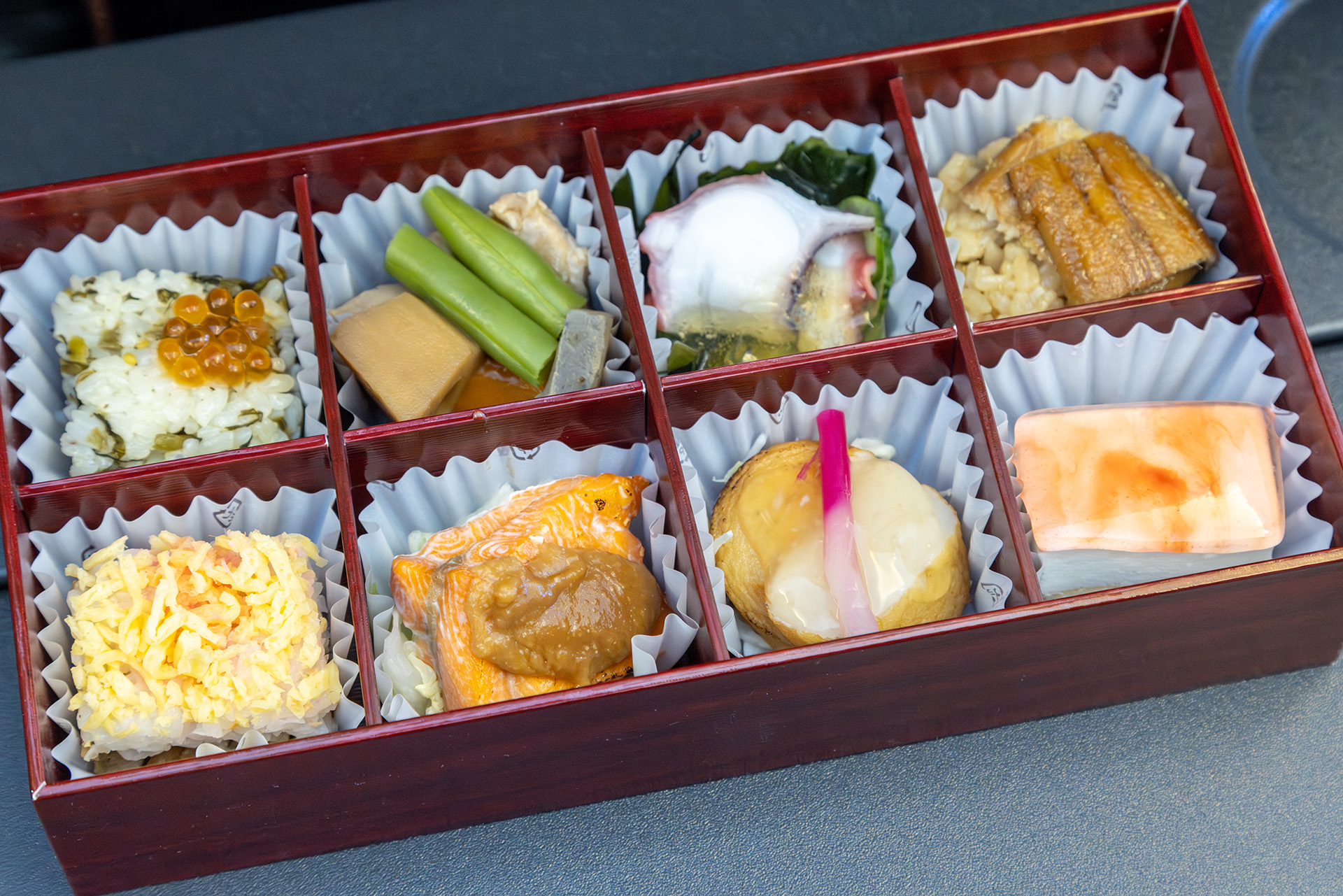 メニューは左上から「高菜押し寿司」「筑前煮（鶏肉、人参、蓮根、蒟蒻、隠元）」「胡瓜と蛸の酢の物」「穴子寿司」「彩しま寿司（酢飯、味付け椎茸、味付け干瓢、錦糸玉子、でんぶ）」「鮭味噌焼き」「薩摩揚げ生姜餡掛け」「あまおうチーズケーキ」