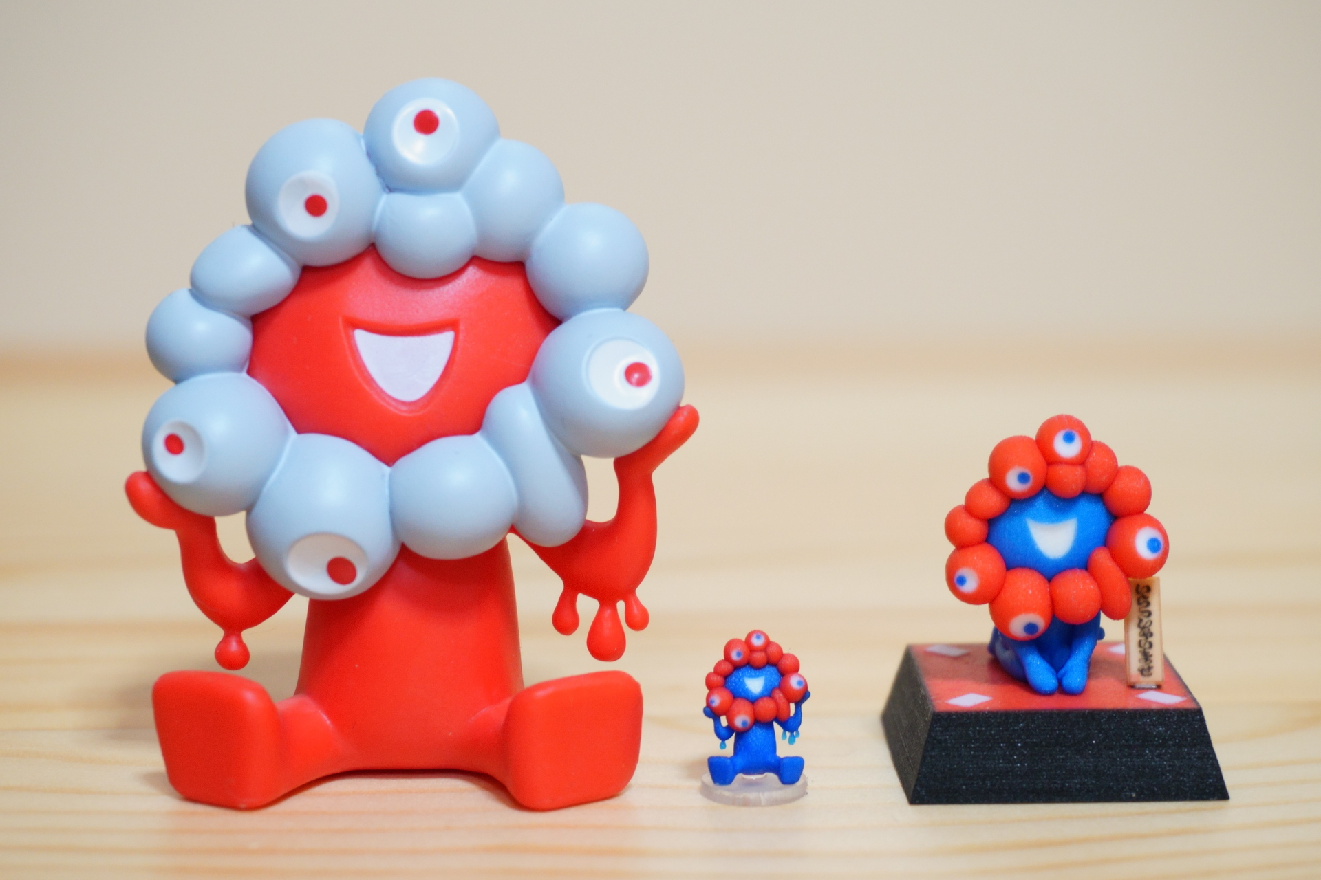 左から海洋堂のミャクミャクカプセルフィギュア おすわり（記者私物）、ビリーヴのミニミニフィギュア、いらっしゃいフィギュア