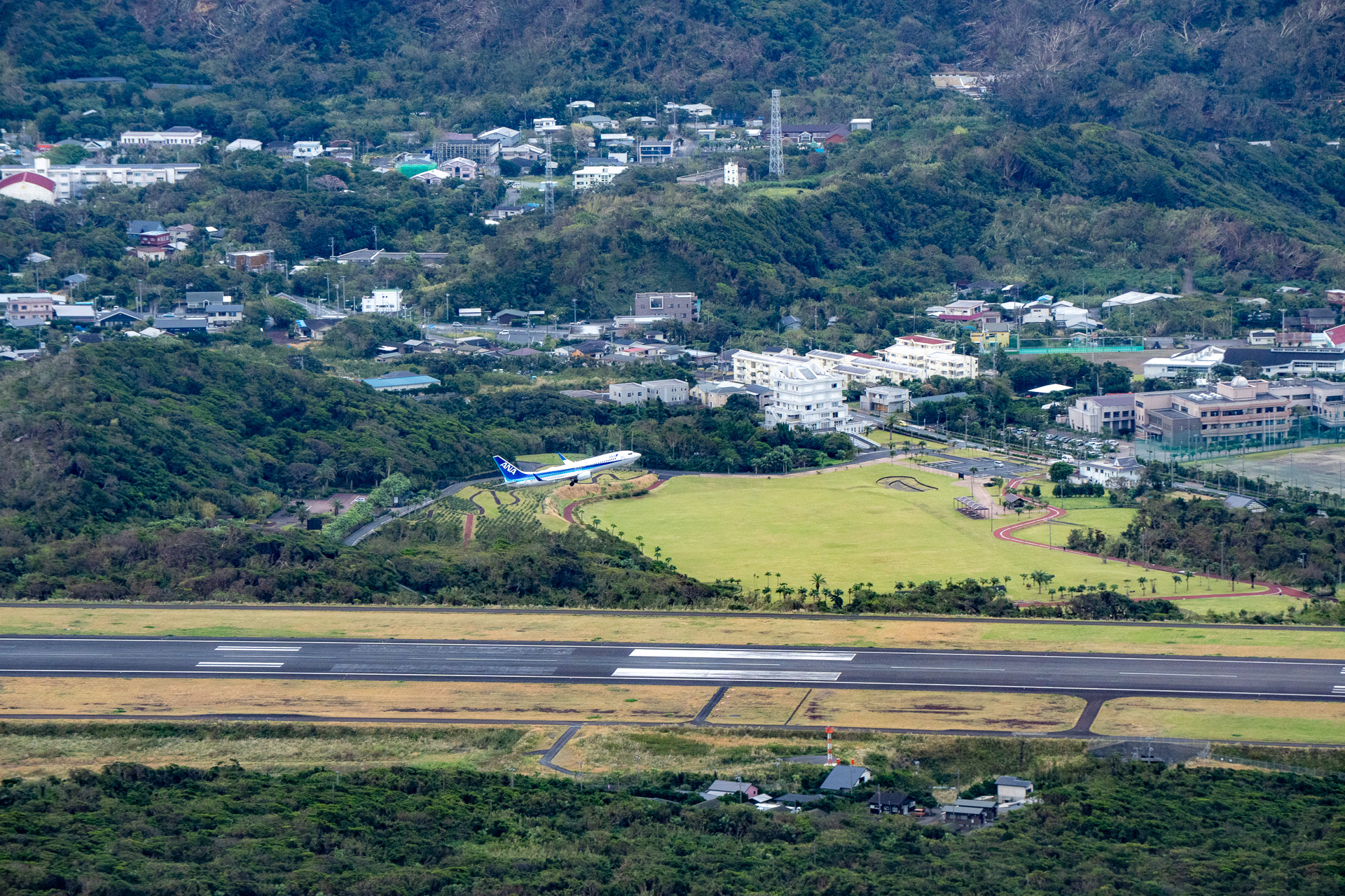 7合目にある「ふれあい牧場展望台」からの眺め。眼下には空港を中心に街並みと海が広がり、今まさに飛び立とうとする飛行機が