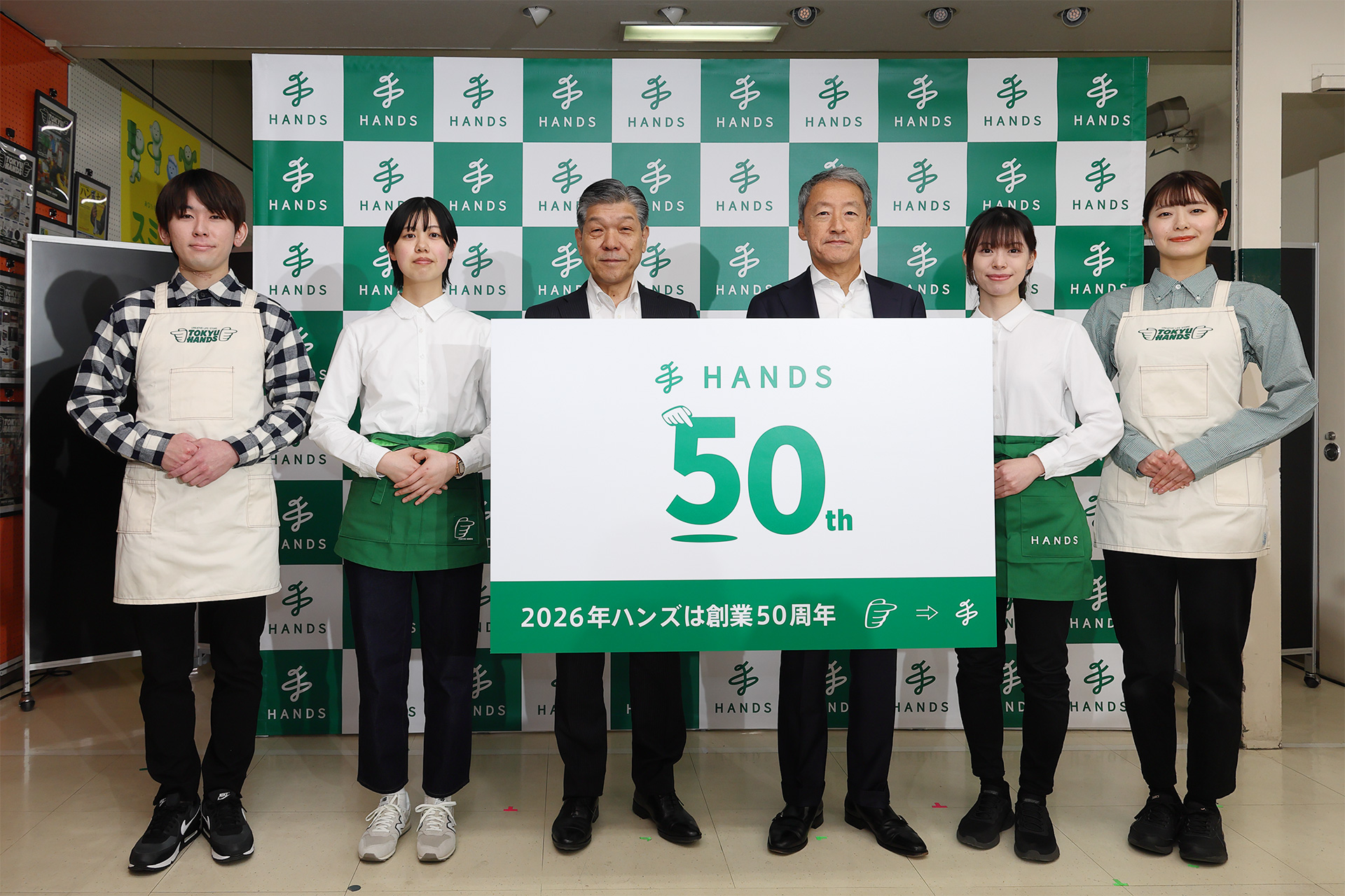 ハンズの高家会長、桜井社長を中心に、歴代ユニフォームをまとった店員らが創業50周年記念ロゴを披露