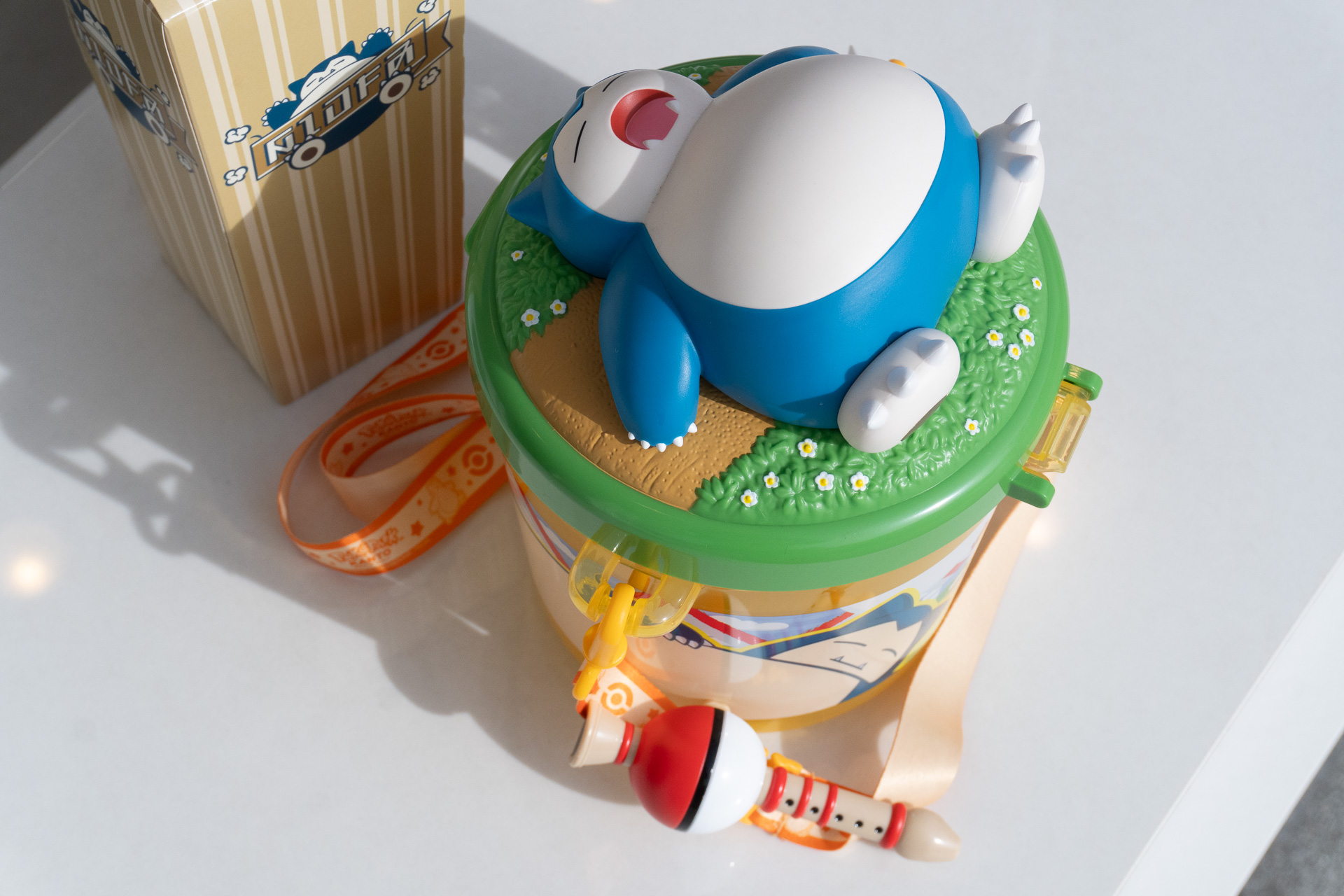 The neck strap features a charm of the "essential item" for waking Snorlax: the Poké Flute.