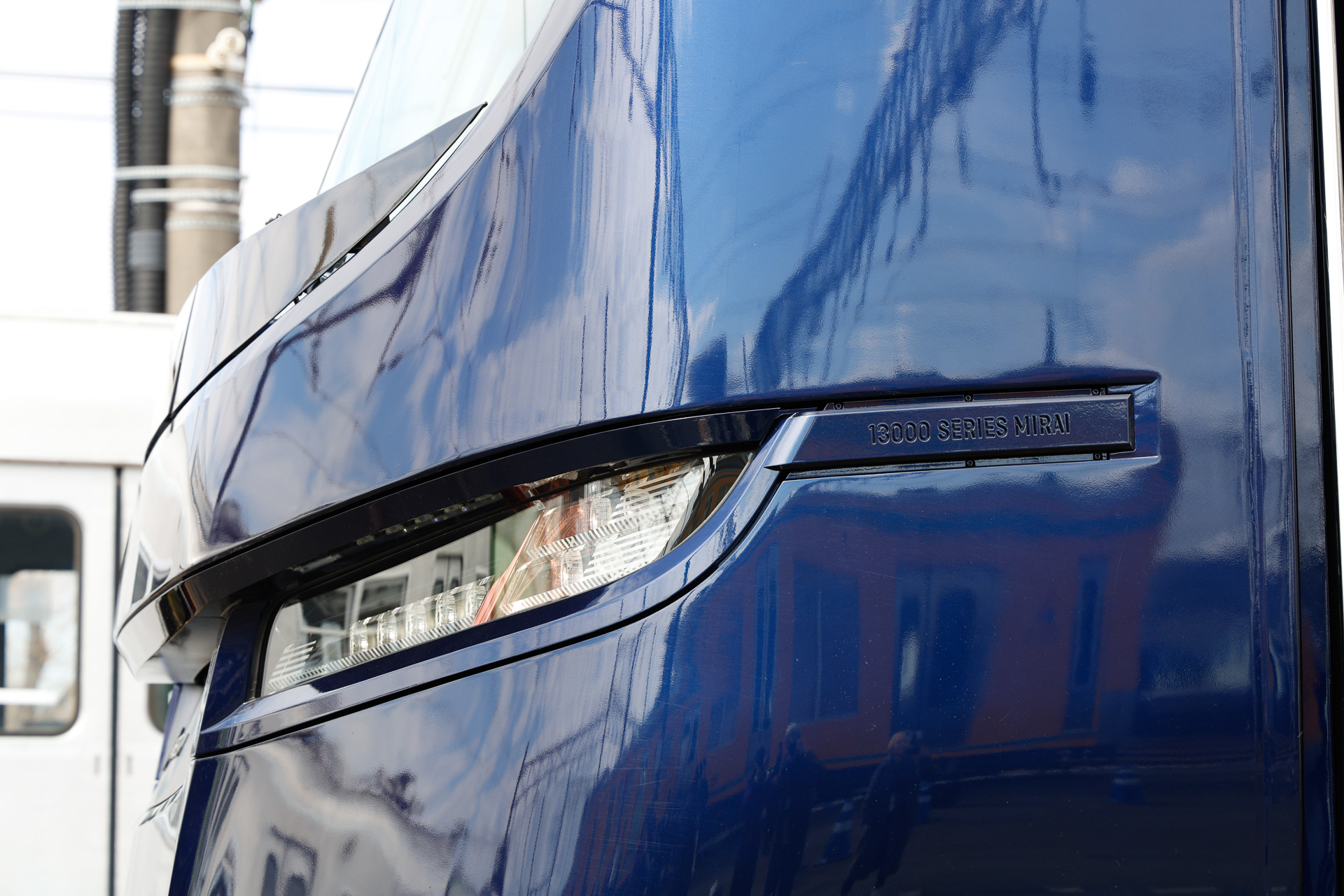 前部標識灯は「未来を見つめる目」と説明される。汎用品の小型LEDを複数組み合わせて、理想的な照度・配光になるように工夫した一品である。その右側にある「13000 SERIES MIRAI」と書かれた部材は、「Concept Emblem」という。実はこれ、前部標識灯を取り付けるためのビスが外から見えないようにするカバーも兼ねている